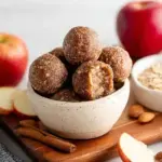 A bowl of round Apple Pie Energy Bites sitting on a wooden kitchen counter.