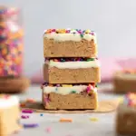 A stack of sliced Birthday Cake Protein Bars with white chocolate drizzle and rainbow sprinkles on parchment paper.