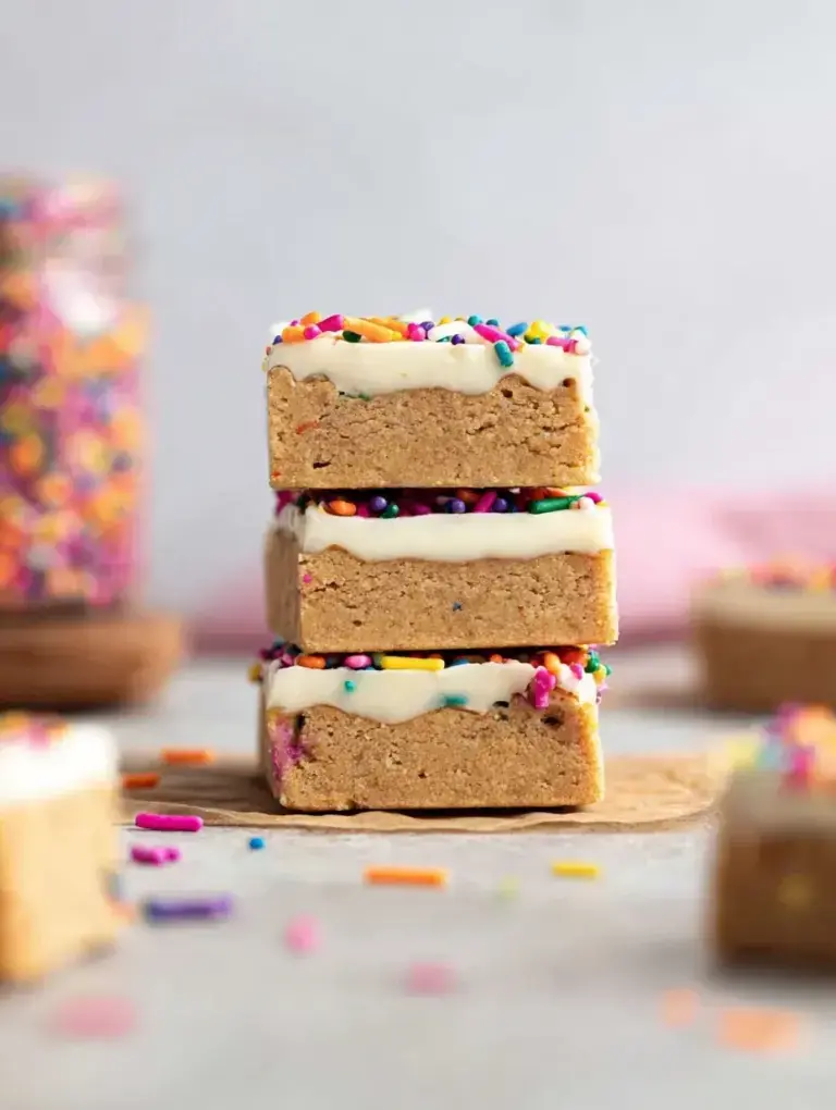 A stack of sliced Birthday Cake Protein Bars with white chocolate drizzle and rainbow sprinkles on parchment paper.