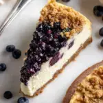 A slice of Blueberry Crumble Cheesecake with purple fruit swirls and golden oat streusel on top