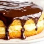 A fresh Boston Cream Pie with chocolate ganache dripping down the sides on a white cake stand.