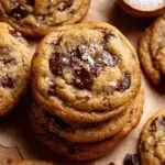 A stack of thick Chewy Pumpkin Chocolate Chip Cookies with melty chocolate chips on a wooden board