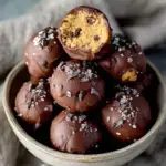 A tray of small round Chickpea Cookie Dough Bites with mini chocolate chips sitting on white parchment paper.