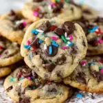 A stack of buttery Chocolate Chip Birthday Cookies with melting chocolate and colorful sprinkles on a cooling rack