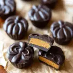 A tray of homemade Chocolate Pumpkin Butter Cups sitting on a wooden board with autumn decorations.