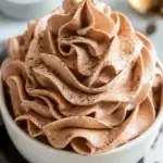 A bowl of fluffy Chocolate Whipped Cream with a whisk and cocoa powder