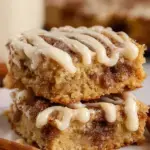 A close up shot of sliced Cinnamon Roll Blondies with a white vanilla glaze drizzle on a piece of parchment paper.