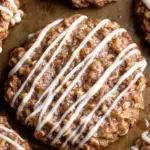 A stack of Cinnamon Roll Oatmeal Cookies drizzled with white vanilla glaze on a cooling rack.