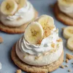 A plate of chilled Crumbl Banana Cream Pie Cookies topped with whipped cream and a vanilla wafer