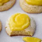A thick Crumbl Lemon Bar Cookie topped with bright yellow lemon curd and a dusting of powdered sugar on a white plate.