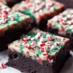 A stack of fudgy Dark Chocolate Peppermint Brownies topped with crushed candy canes on a festive plate.