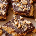 A tray of chocolate-covered Date Snickers sprinkled with sea salt on parchment paper