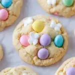 A pile of soft Easter M&M Cookies with pastel pink and blue chocolate candies on a white plate.