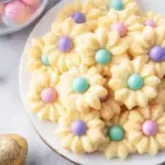 A tray of colorful Easter Spritz Cookies in shapes of eggs and flowers on a white plate