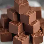 A close up shot of square pieces of Easy Chocolate Fudge stacked on a wooden board.