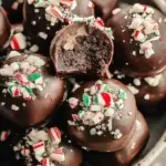 White chocolate coated peppermint gluten free oreo truffles topped with crushed candy canes on a white plate