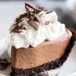 A slice of French Silk Pie topped with fresh whipped cream and chocolate shavings on a white plate.
