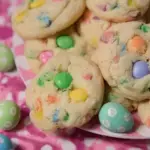 A stack of Funfetti Easter M&M Cookies with pastel chocolate candies and colorful sprinkles on a white plate.