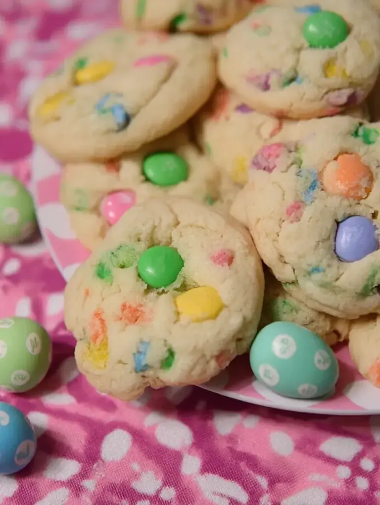 A stack of Funfetti Easter M&M Cookies with pastel chocolate candies and colorful sprinkles on a white plate.