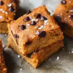 A stack of chewy Gluten-Free Blondies with melty chocolate chips on a wooden board.