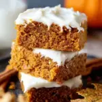 A close up of sliced Gluten-Free Pumpkin Squares with thick cream cheese frosting on a wooden board