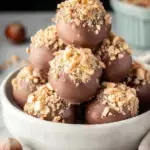 Close up of several chocolate hazelnut truffles coated in chopped nuts on a wooden tray