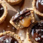 A tray of Healthy Twix Cookie Cups with golden shortbread bases and dark chocolate tops sprinkled with sea salt.
