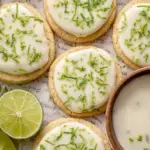 A plate of white powdered sugar coated Key Lime Cookies with visible crinkle cracks and lime zest.