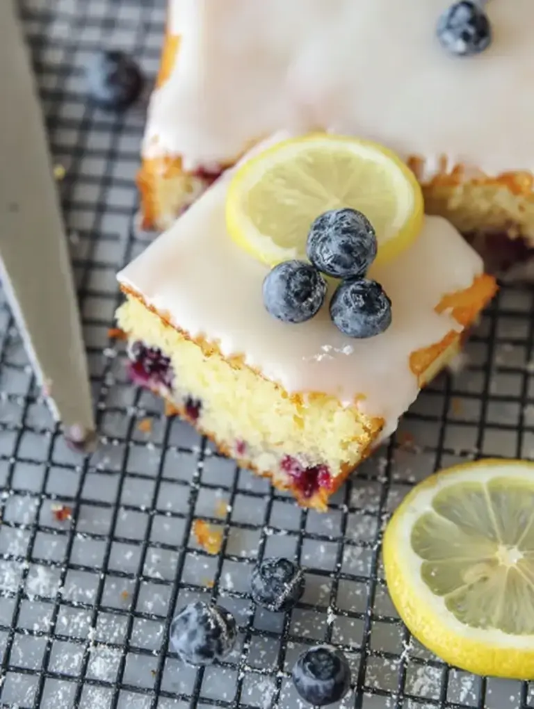 A slice of Lemon Blueberry Sheet Cake with thick cream cheese frosting and fresh berries