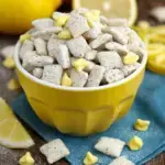 A bowl of powdered sugar coated lemon muddy buddies snack mix on a kitchen counter