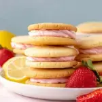 Two lemon sandwich cookies with pink strawberry frosting filling on a white plate