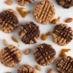 A plate of dense, healthy no bake almond butter cookies with mini dark chocolate chips on a wooden table.