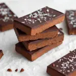 A rectangular slab of No-Bake Chocolate Protein Bars being cut on parchment paper.
