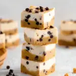 A close up shot of sliced no-bake cookie dough cheesecake bars with a thick chocolate ganache layer on top