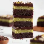 A close-up shot of sliced No-Bake Dubai Chocolate Brownies showing the bright green pistachio and crunchy kataifi layer.