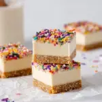 A square of No-Bake Funfetti Cheesecake Bars with rainbow sprinkles on a white plate