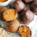 A plate of round No-Bake Pumpkin Bites with mini chocolate chips sitting on a wooden table.