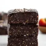 A square of dark, fudgy No-Bake Vegan Brownies topped with chocolate chips on a wooden board.