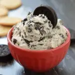 A bowl of creamy Oreo Cookie Dough with crushed cookies and a silver spoon.