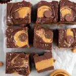 A close-up shot of square pieces of Peanut Butter Cup Fudge showing the distinct peanut butter and chocolate layers topped with chopped candy.