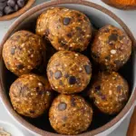 A tray of round Pumpkin Energy Balls with mini chocolate chips arranged in a cozy kitchen setting.