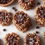Small clusters of dark chocolate quinoa crisps topped with flaky sea salt on a parchment lined tray