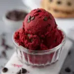 A bowl of vibrant Red Velvet Edible Cookie Dough with mini chocolate chips and a spoon