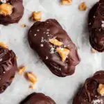 A tray of chocolate-covered Snickers Dates topped with sea salt and whole peanuts.