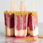 Homemade Strawberry Cheesecake Popsicles with red fruit swirls and graham cracker crumbs
