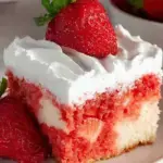 A slice of Strawberry Poke Cake with fresh strawberry slices on top and white whipped frosting.