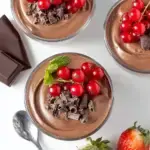 A glass ramekin filled with smooth dark Tofu Chocolate Mousse topped with a fresh raspberry.