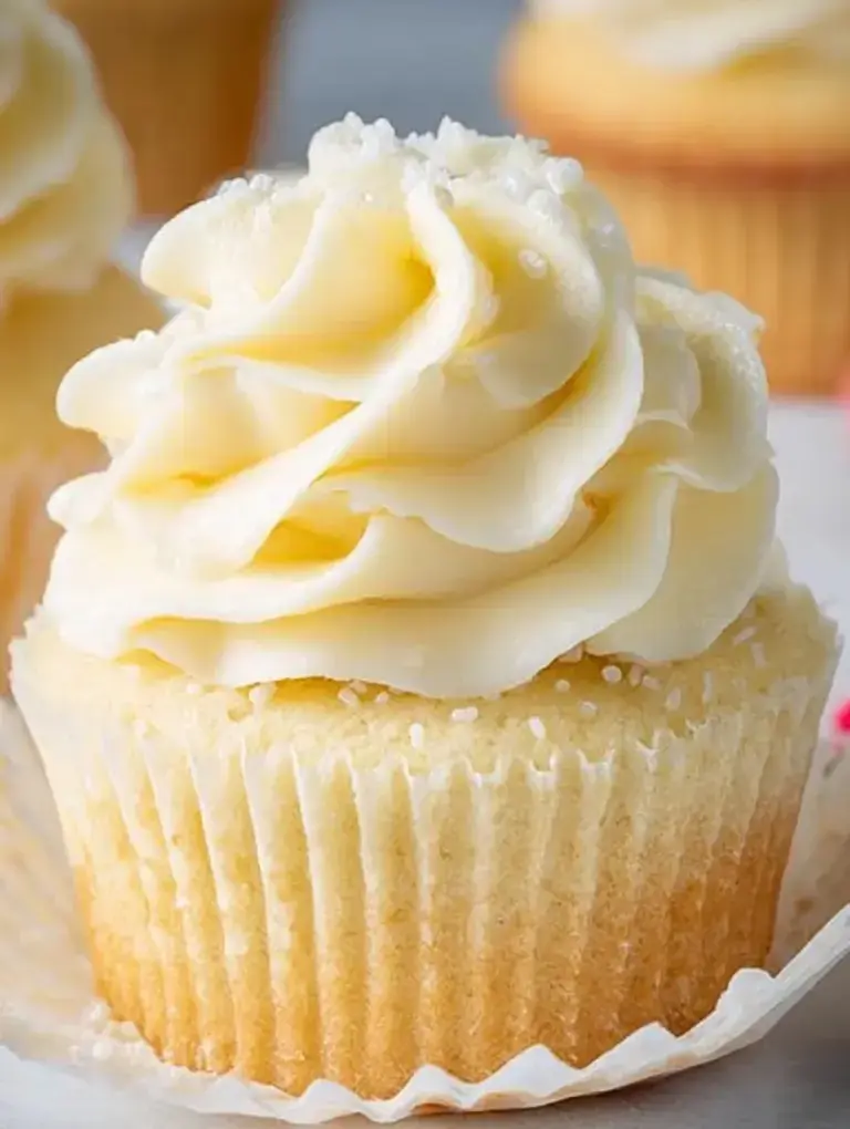 A batch of Classic Vanilla Cupcakes topped with smooth vanilla buttercream frosting and sprinkles.