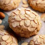 A tray of golden brown Vegan Almond Cookies topped with sliced almonds on a cooling rack