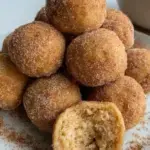 A plate of golden brown Vegan Apple Cider Donut Holes coated in cinnamon sugar.